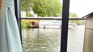 A room with a large window overlooking a canal, a wicker chair with a cushion, and a book titled "Lust auf Meer".