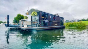 A floating houseboat with a deck, windows, and a small garden area.