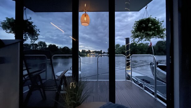 A covered outdoor area with a view of a river, metal railings, and a hanging light fixture.