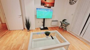 A living room with a television, a coffee table, a plant, and a wall clock.