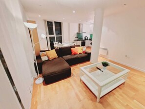 A modern living room with a brown sectional sofa, a glass coffee table, and a white floor lamp. - Deluxe 2-bed Apartment Near Shoreditch (London)