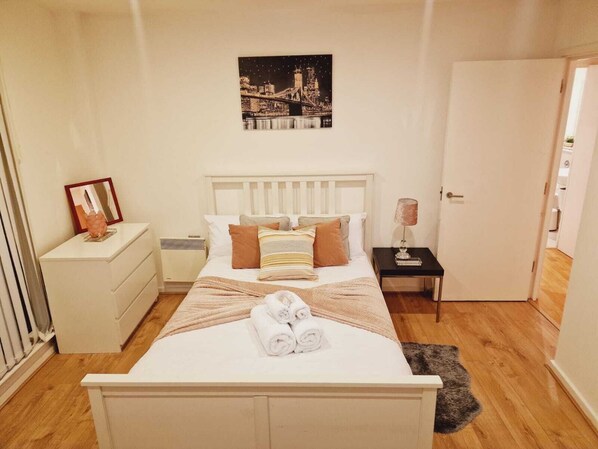 A neatly arranged bedroom with a bed, bedside tables, a nightstand, a framed picture, and a door. - Deluxe 2-bed Apartment Near Shoreditch (London)