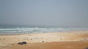 A beach with people and vehicles, and a clear view of the ocean. - Oasis Seaside by Barok (Dakar)