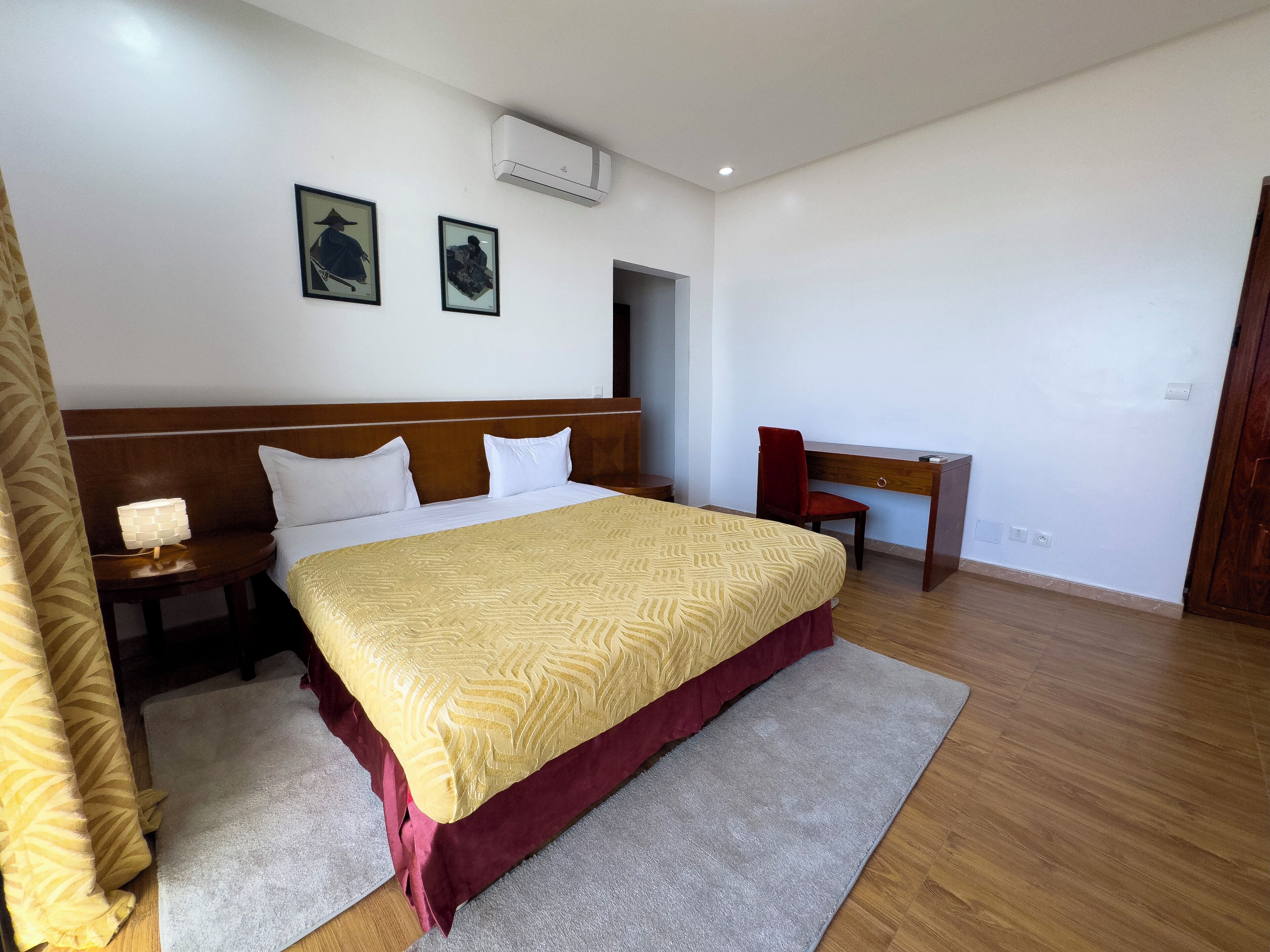 A hotel room with a large bed, a desk, and two wall-mounted air conditioning units.