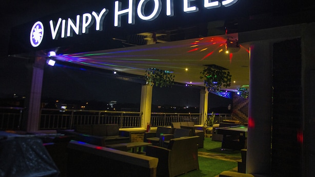 Señal de Vinpy Hotels con mesas al aire libre y vista de la ciudad de noche.