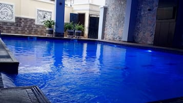 Una piscina interior con un elemento acuático azul, paredes de piedra y plantas en macetas.