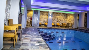 Una piscina interior moderna con escalones escalonados, paredes de piedra y sillones de descanso.