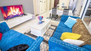 A living room with a TV, blue sofa, coffee table, and patterned rug. - Lavington View Palace Apartment  Kenya (Nairobi)