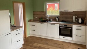 Una cocina con armarios blancos, encimera de madera y ventana con vista a un edificio rojo.