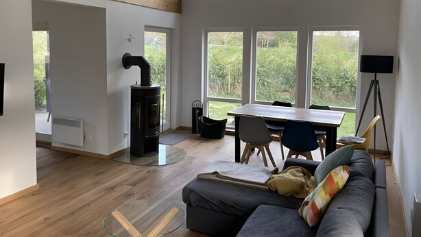 Una sala moderna con estufa de leña integrada, ventanas amplias, comedor y sofá.
