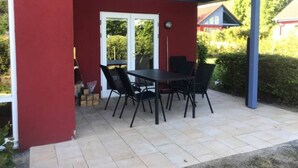 Un patio techado con una mesa y sillas, una puerta y vistas del entorno.