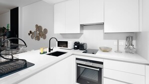 Une cuisine moderne avec des meubles blancs, un four encastré, un four à micro-ondes et un évier.