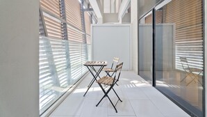 Un balcon moderne avec une paroi en verre, une table en bois et une chaise.