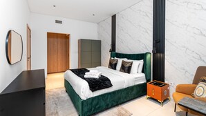 Une chambre à coucher moderne avec un lit recouvert d’un tissu vert, une armoire en bois, un mur en marbre et une petite table d’appoint orange.