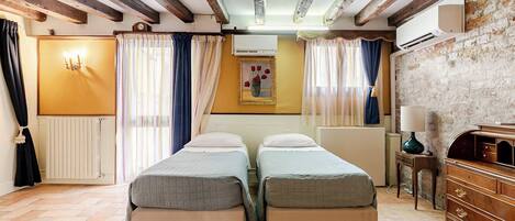 A room with two beds, a radiator, a wooden dresser, and a brick wall.