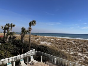 Une vue sur la plage avec une terrasse en bois, des palmiers et une clôture blanche.