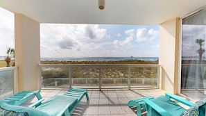 Un balcon donnant sur la plage, agrémenté d’une balustrade et de plusieurs fauteuils de jardin verts.