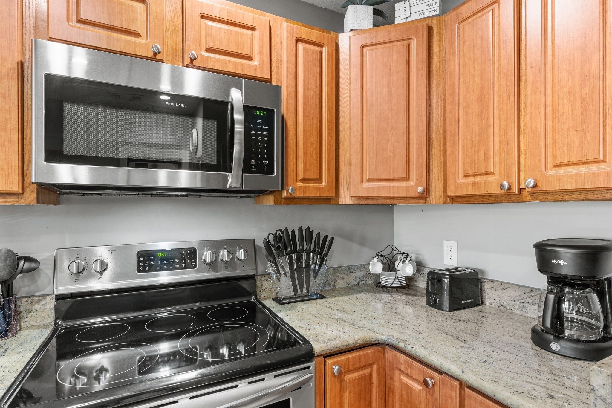 A kitchen with wooden cabinets, a stainless steel microwave, a stove, and a coffee maker.