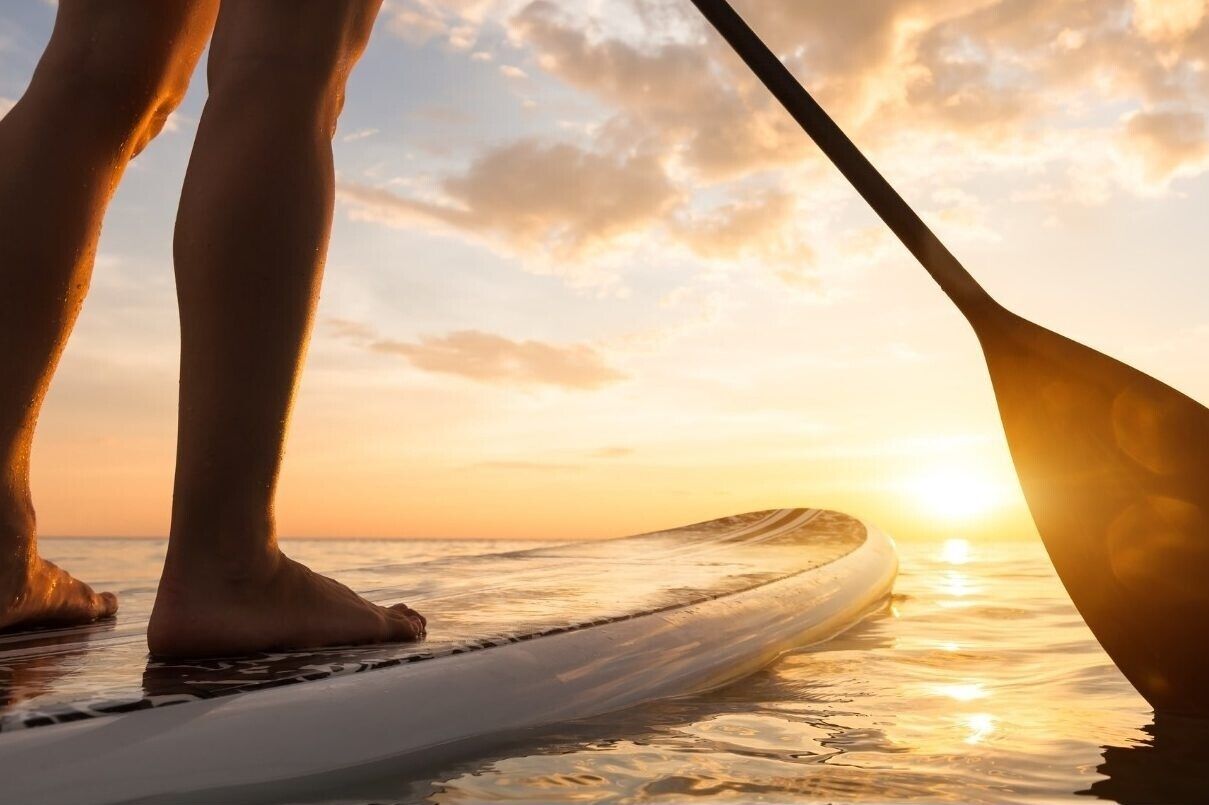 A person standing on a surfboard at the beach during sunset.