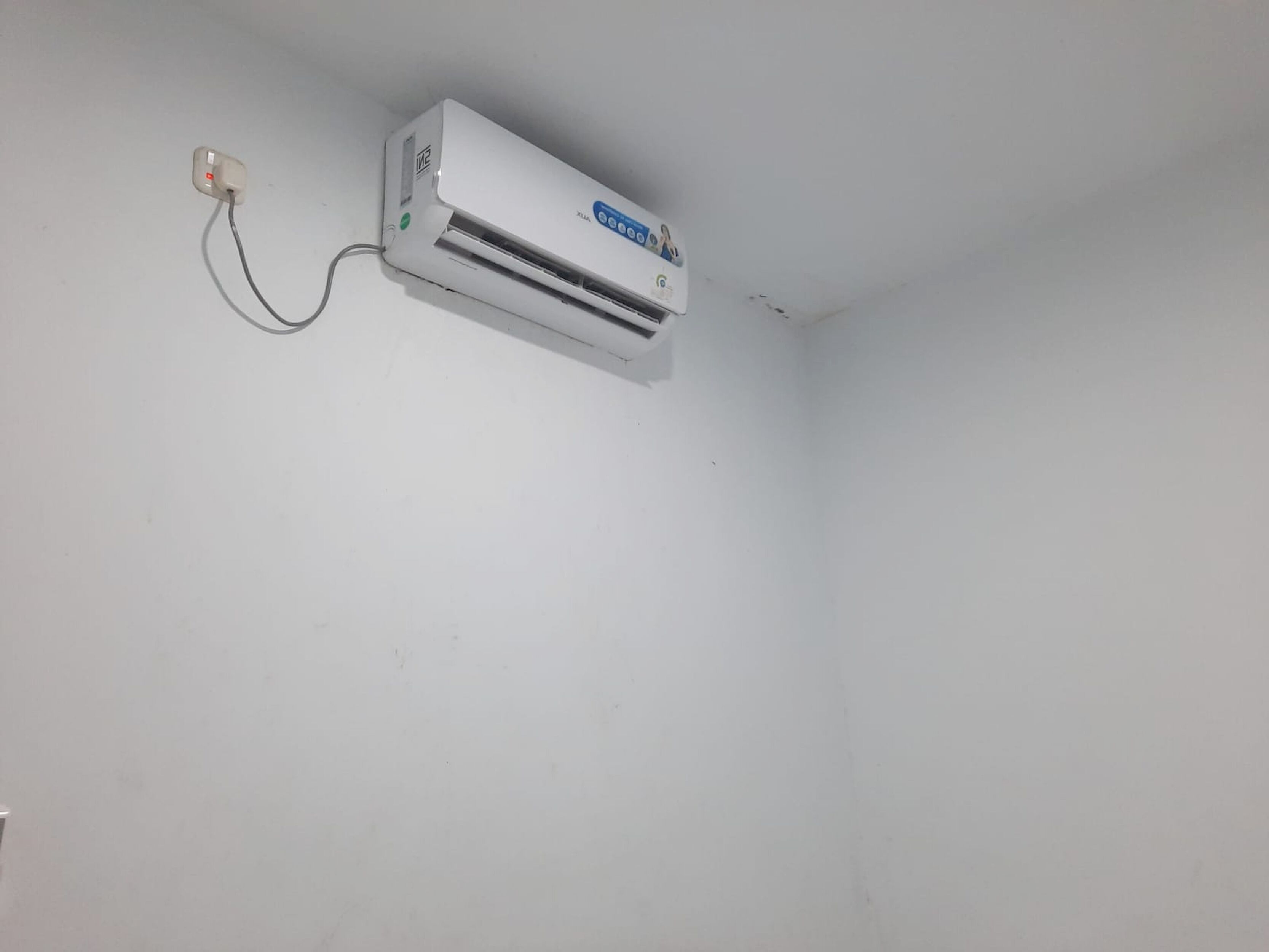 Un appareil de climatisation blanc, fixé au mur, avec un câble d’alimentation visible.