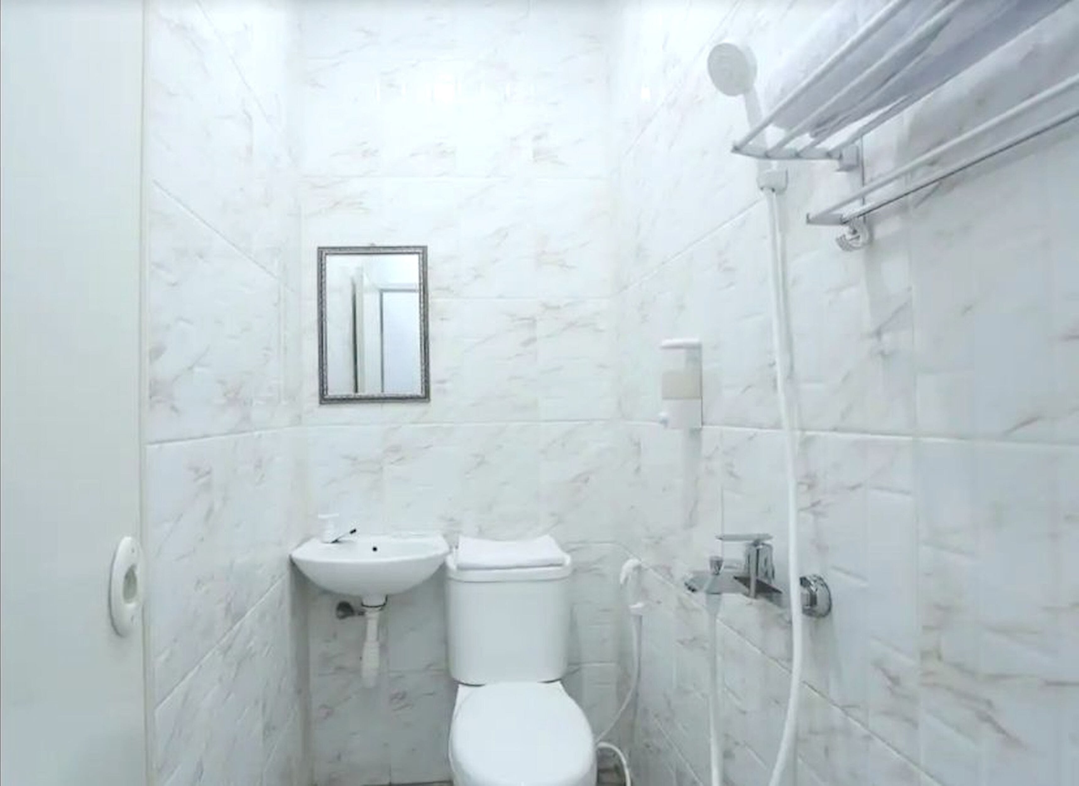 A small, white bathroom with a toilet, sink, and shower.