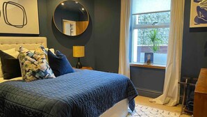 Una camera da letto con un letto, uno specchio tondo, una finestra con tende e una pianta sul davanzale.
