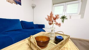 A modern living room with a blue sofa, a wooden coffee table with a woven basket, a vase with pink foliage, and a floor lamp.