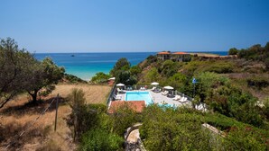 Zona de piscina con vistas al mar, rodeada de vegetación y una ladera.