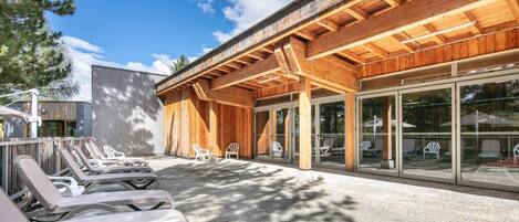 A modern building with a wooden facade and large glass windows. There are outdoor lounge chairs and a concrete patio area.