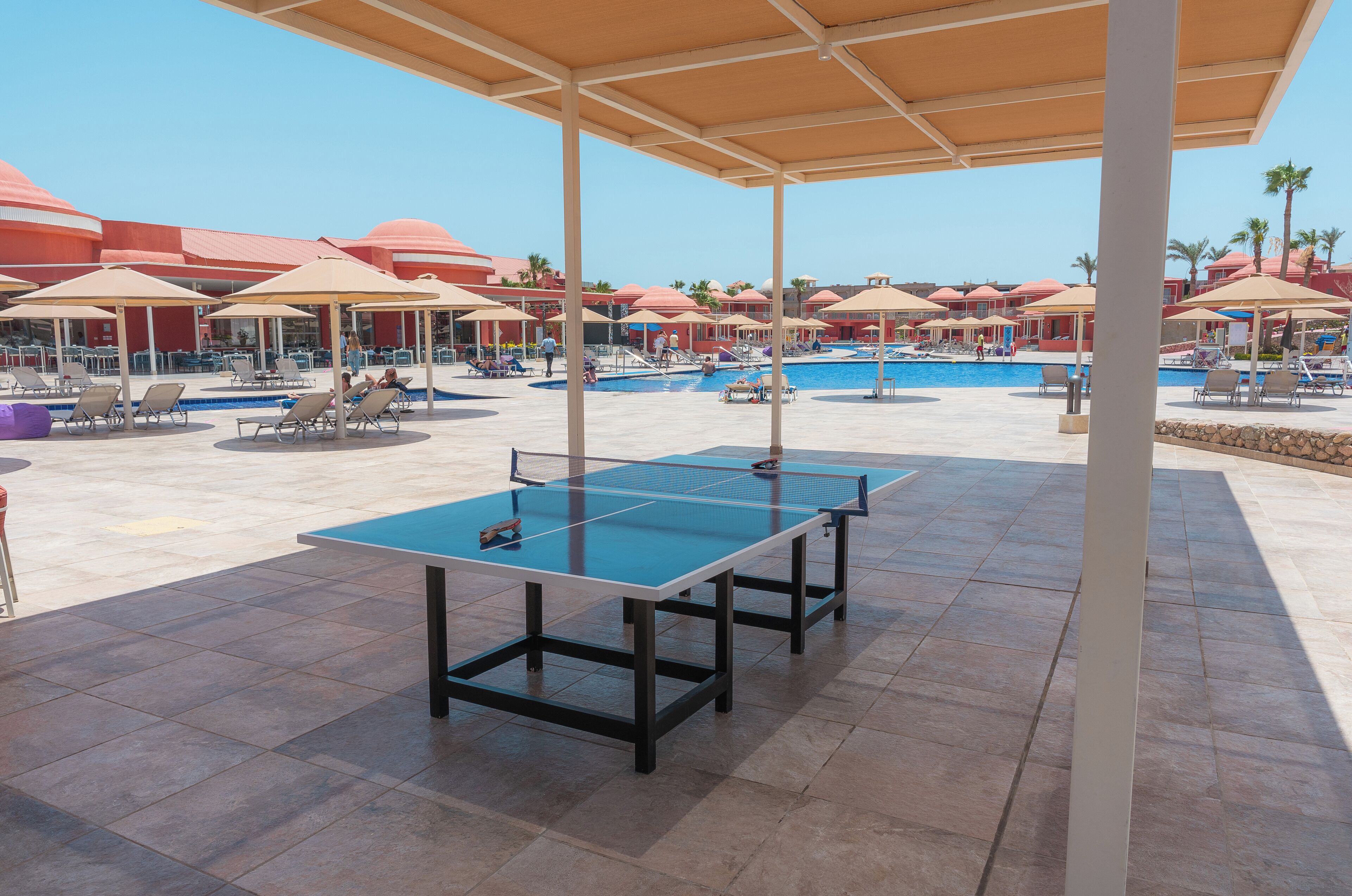 An outdoor pool area with lounge chairs, umbrellas, and a ping pong table.