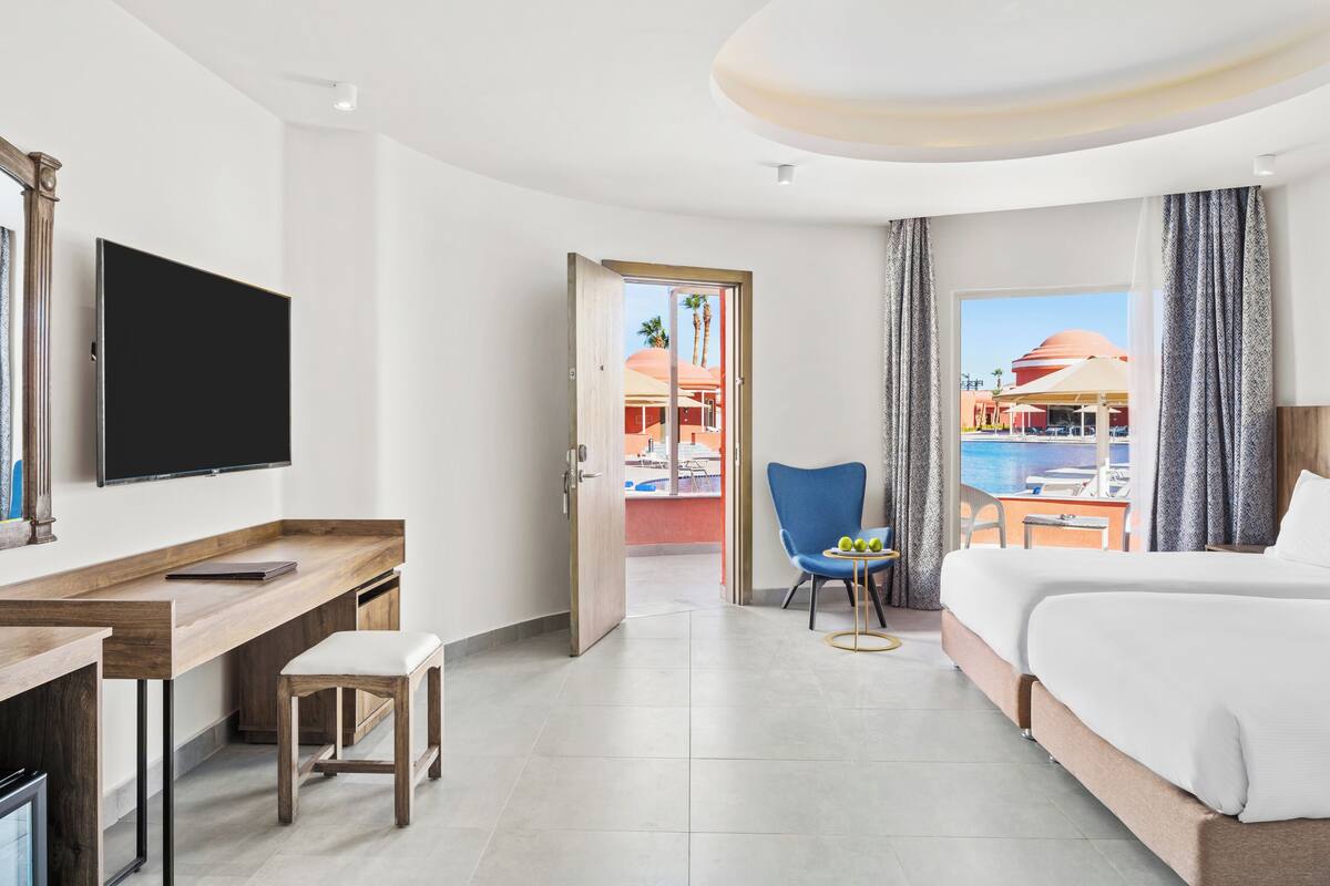 Une chambre d’hôtel comprenant un lit, un bureau avec une chaise, une télévision et une vue sur une piscine et un bâtiment situés à l’extérieur.