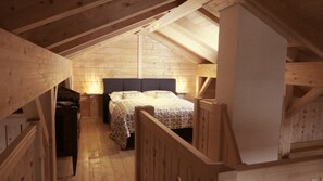Une chambre mansardée en bois, avec un lit, des tables de chevet et un escalier en bois.