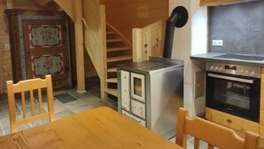 A compact kitchen with a stove, oven, and a small refrigerator. A wooden staircase leads to an upper level.