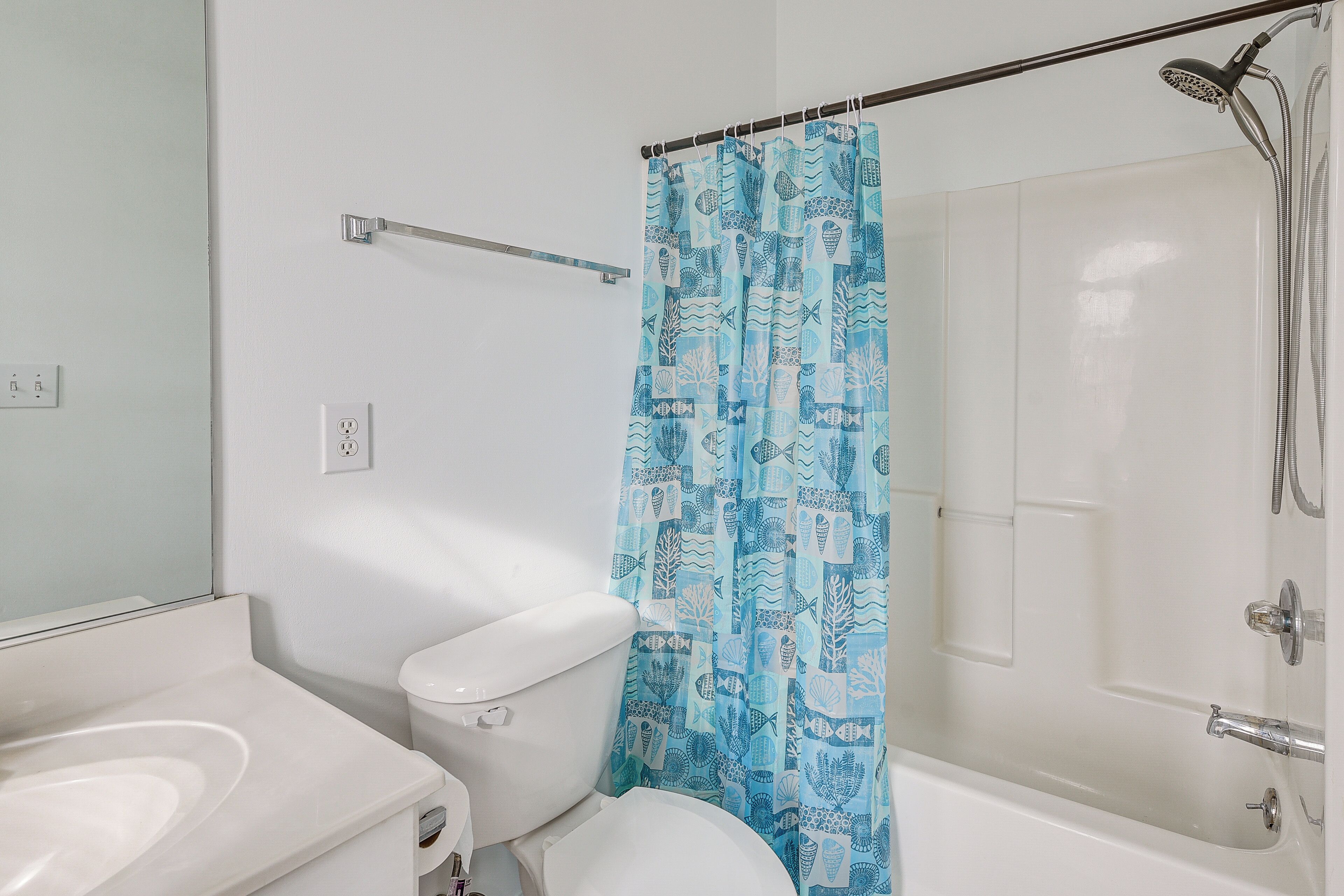 A bathroom with a toilet, a sink, a shower, and a curtain with a pattern.