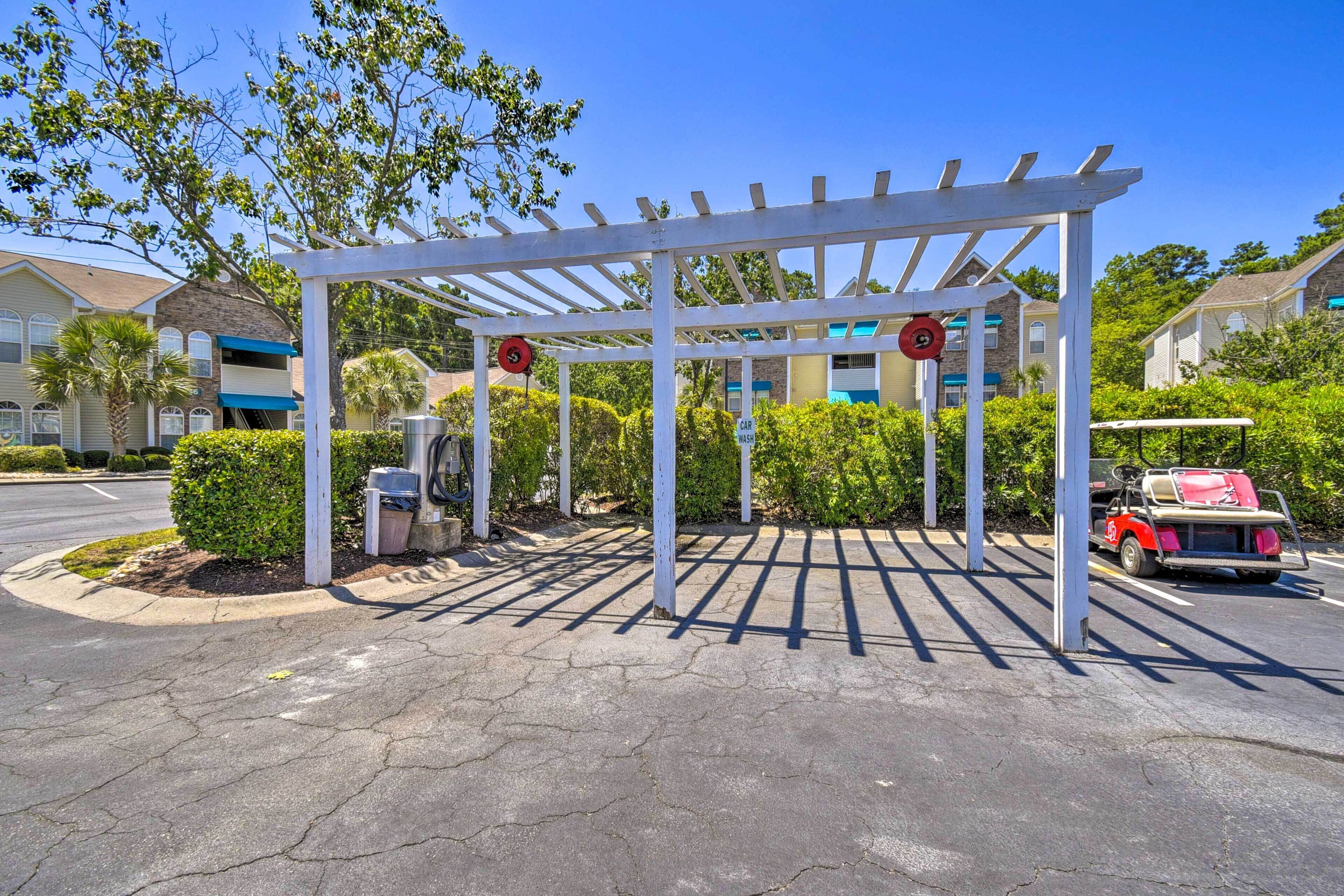 Un espace de stationnement couvert avec une structure de pergola blanche, une voiture rouge et un bâtiment en arrière-plan.