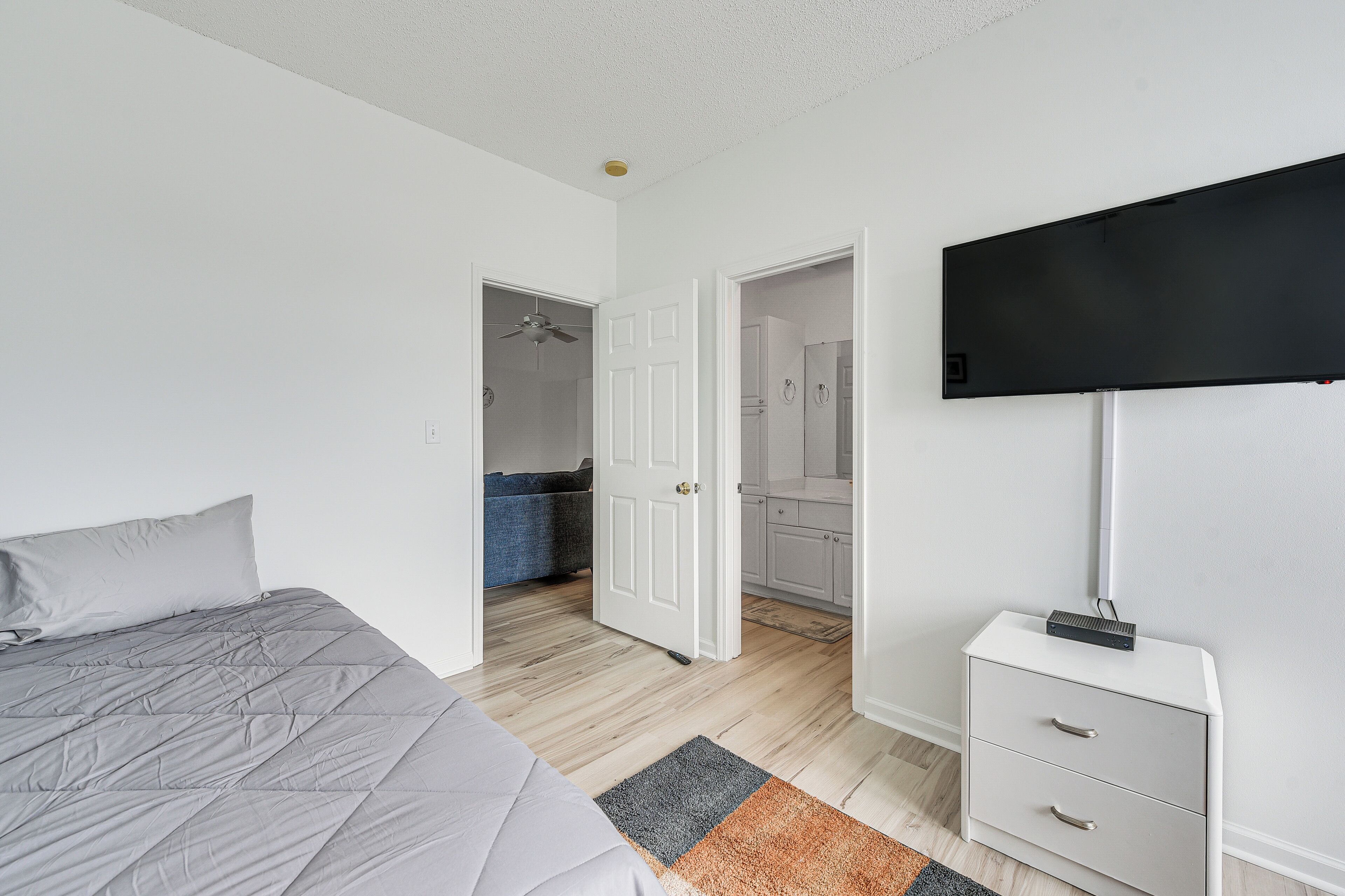 Un dormitorio con cama, mesita de noche, televisor y baño visible a través de una puerta abierta.