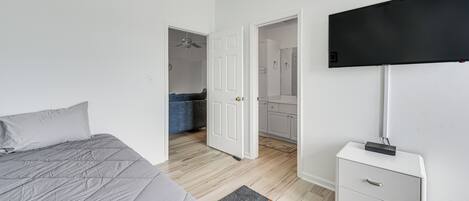Un dormitorio con cama, mesita de noche, televisor y baño visible a través de una puerta abierta.