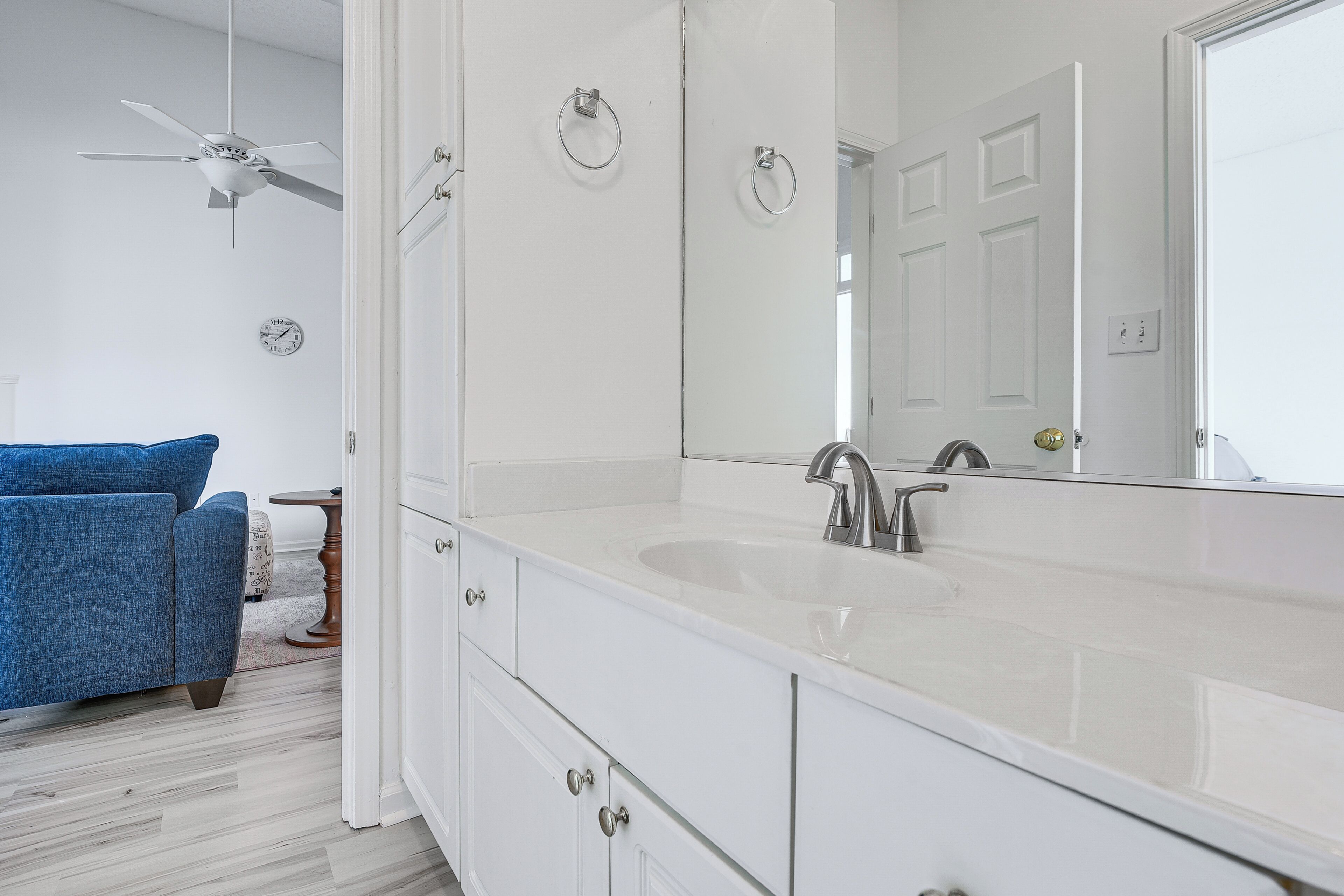 Une salle de bain avec un meuble-lavabo blanc, un grand miroir et un ventilateur de plafond.