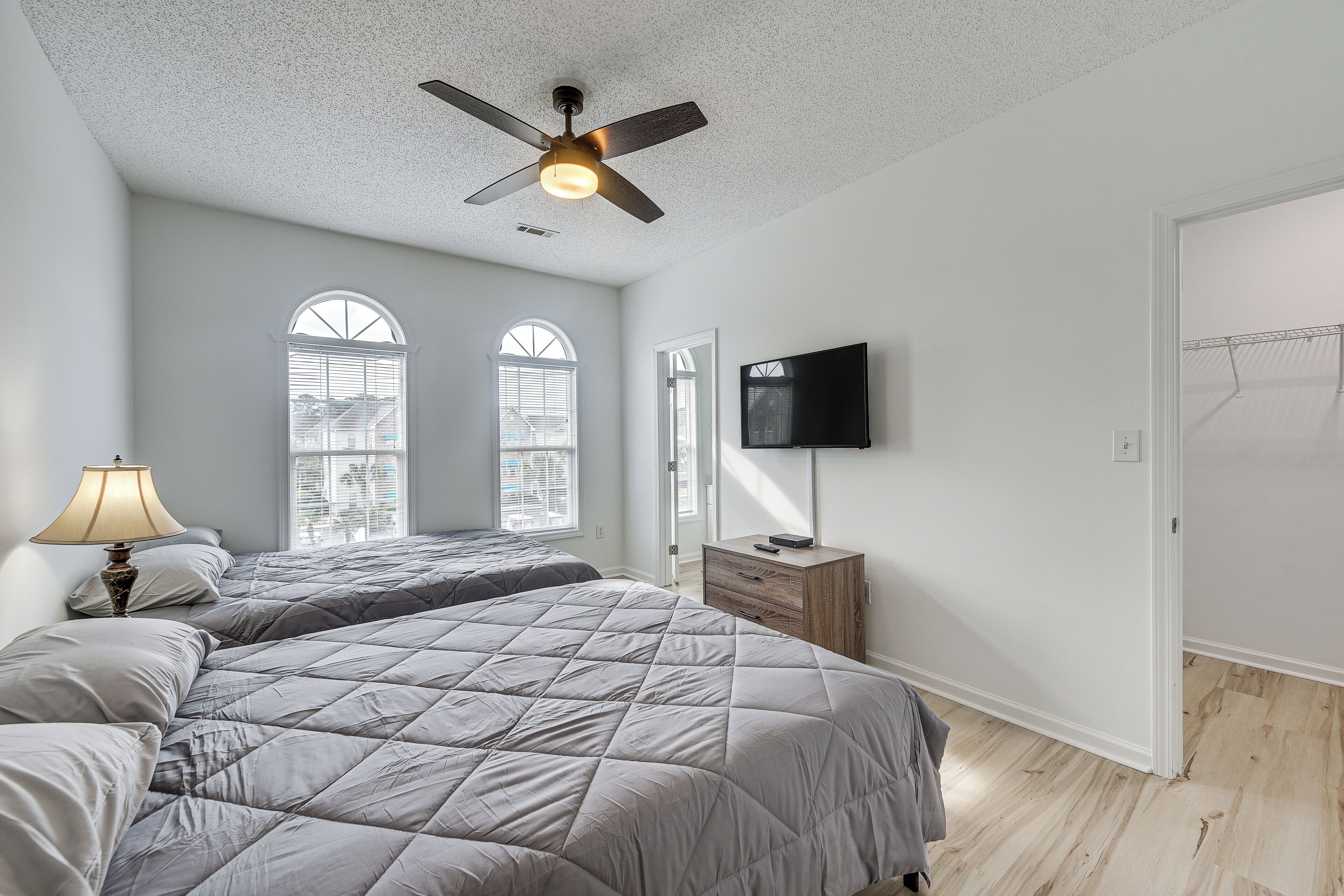 A bedroom with two beds, a ceiling fan, a TV, and a window with blinds.