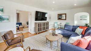 Ein Wohnzimmer mit einem blauen Sofa, Holzstühlen, einem Fernseher und einem Schrank.