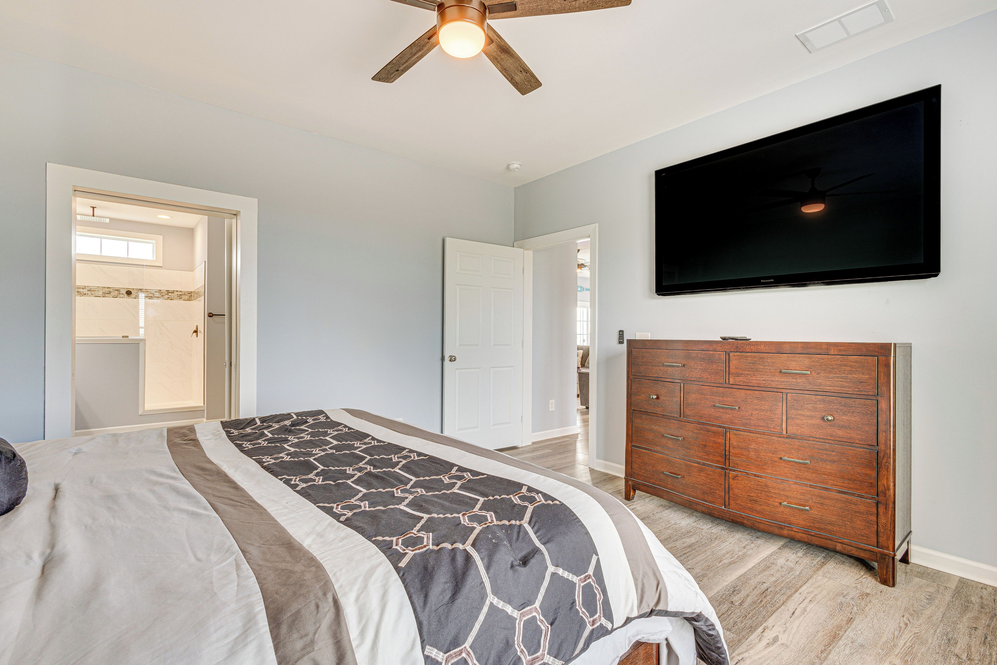 A bedroom with a bed, a dresser, a ceiling fan, and a TV on the wall.