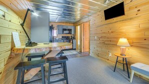 A cozy cabin interior with a wooden interior, a kitchenette, a dining area, and a TV mounted on the wall. - Oscoda Cabin w/ Charcoal Grill: Walk to Lake Huron (Oscoda)