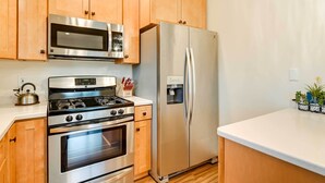 A kitchen with wooden cabinets, stainless steel appliances including a microwave, oven, and refrigerator, and a white countertop. - Soldotna Fishing Cabin ~ Half-mi to Kenai River! (Soldotna)