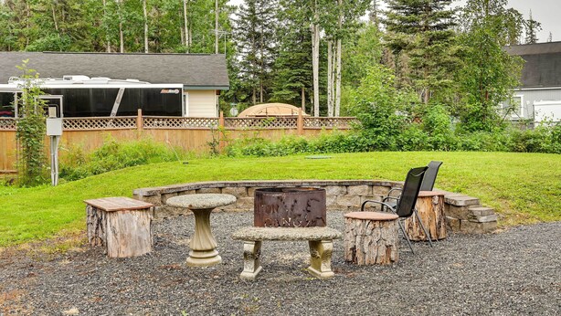 A rustic outdoor seating area with a stone table and benches, surrounded by a wooden fence and a gravel path. - Soldotna Fishing Cabin ~ Half-mi to Kenai River! (Soldotna)