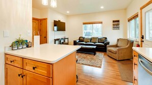 A spacious living area with a kitchen, wooden cabinets, a dining table, and a sofa. - Soldotna Fishing Cabin ~ Half-mi to Kenai River! (Soldotna)