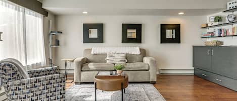 A modern living room with a patterned armchair, a sofa, a coffee table, and a bookshelf.