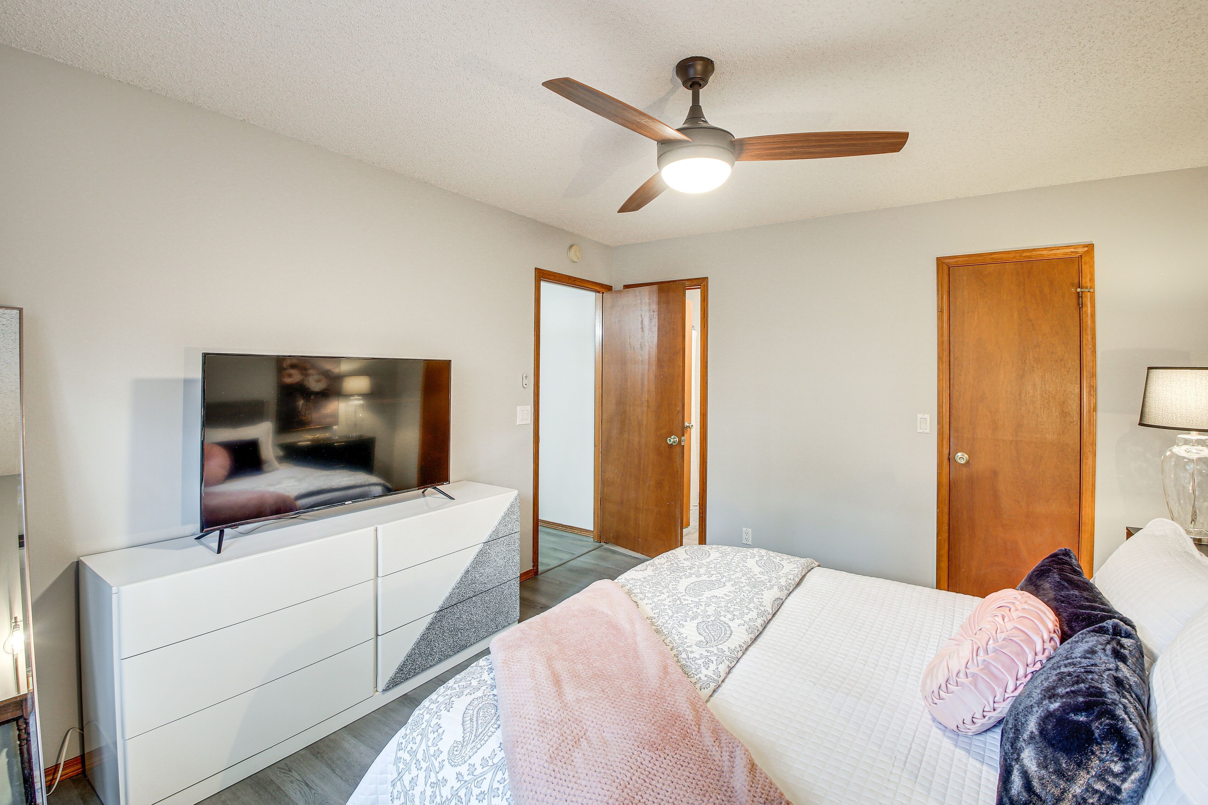 A bedroom with a bed, a TV on a dresser, a ceiling fan, and wooden doors.