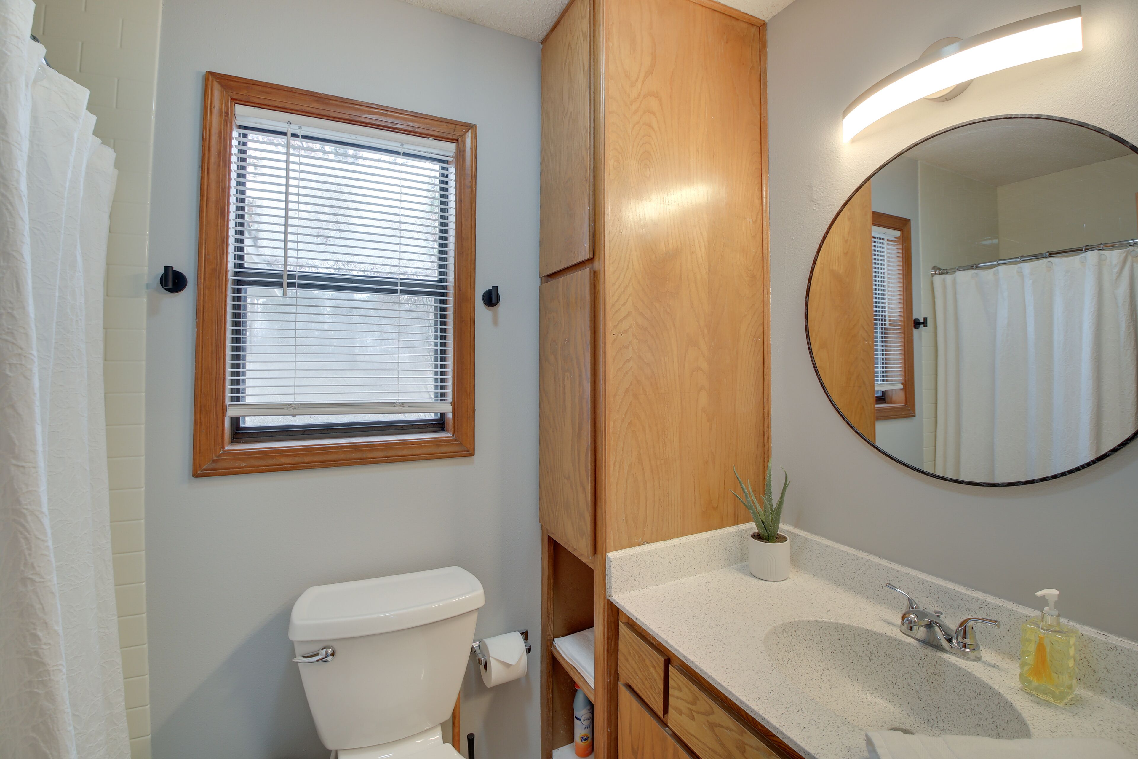 A bathroom with a toilet, a sink, a mirror, and a window with blinds.