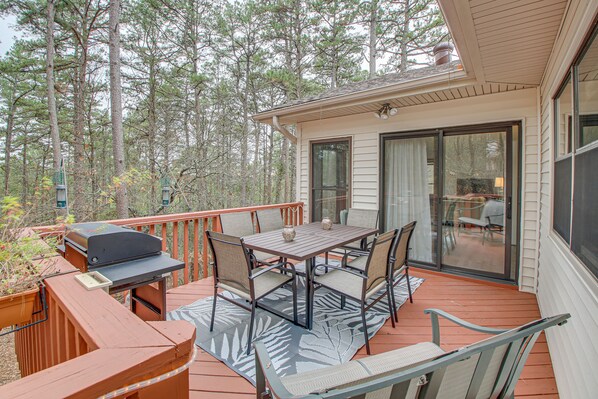A deck with a table and chairs, a grill, and a glass door leading to a patio.
