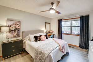 A bedroom with a bed, a dresser, a ceiling fan, a window with curtains, and a painting on the wall.
